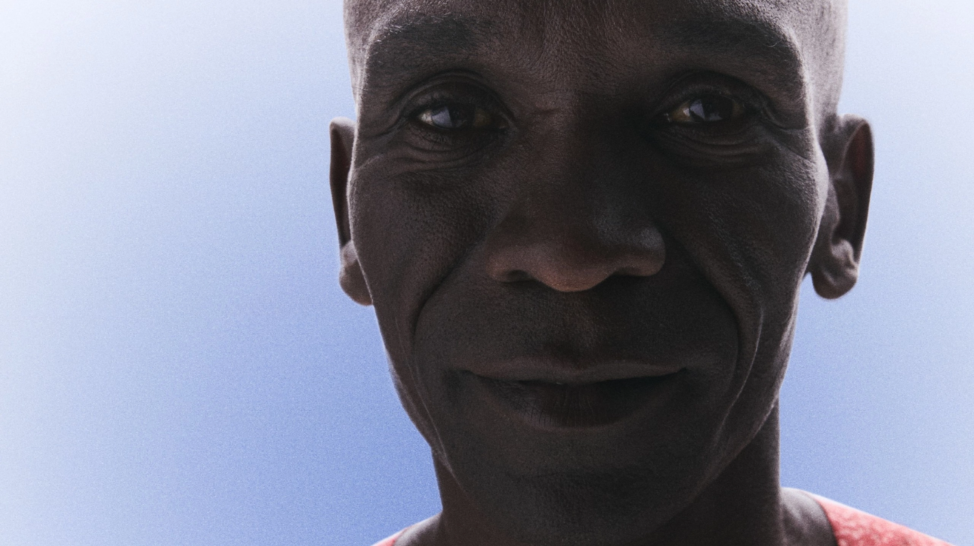 Front upper body view of Eliud Kipchoge smiling and wearing his Kenya track and field kit uniform.