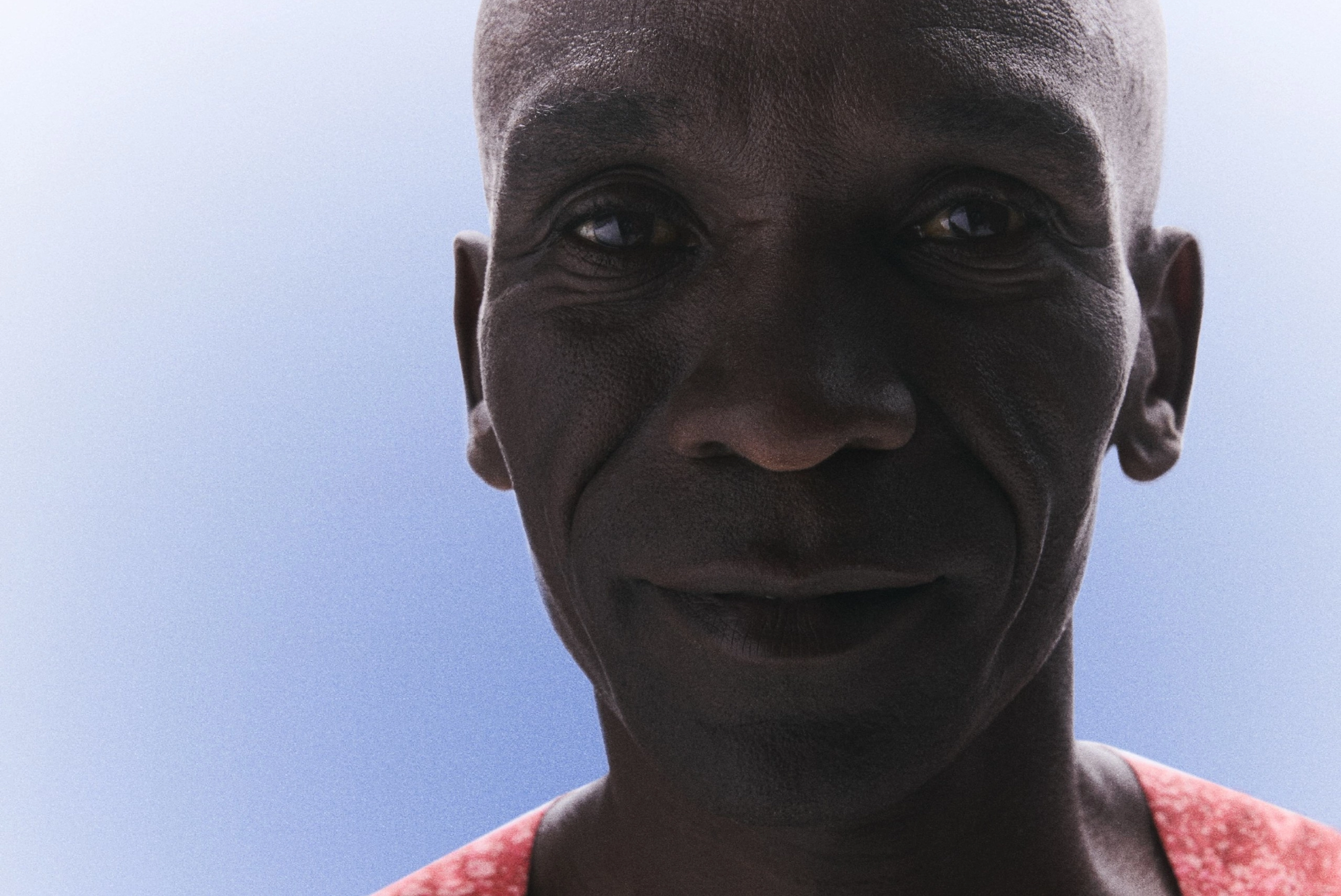 Front upper body view of Eliud Kipchoge smiling and wearing his Kenya track and field kit uniform.