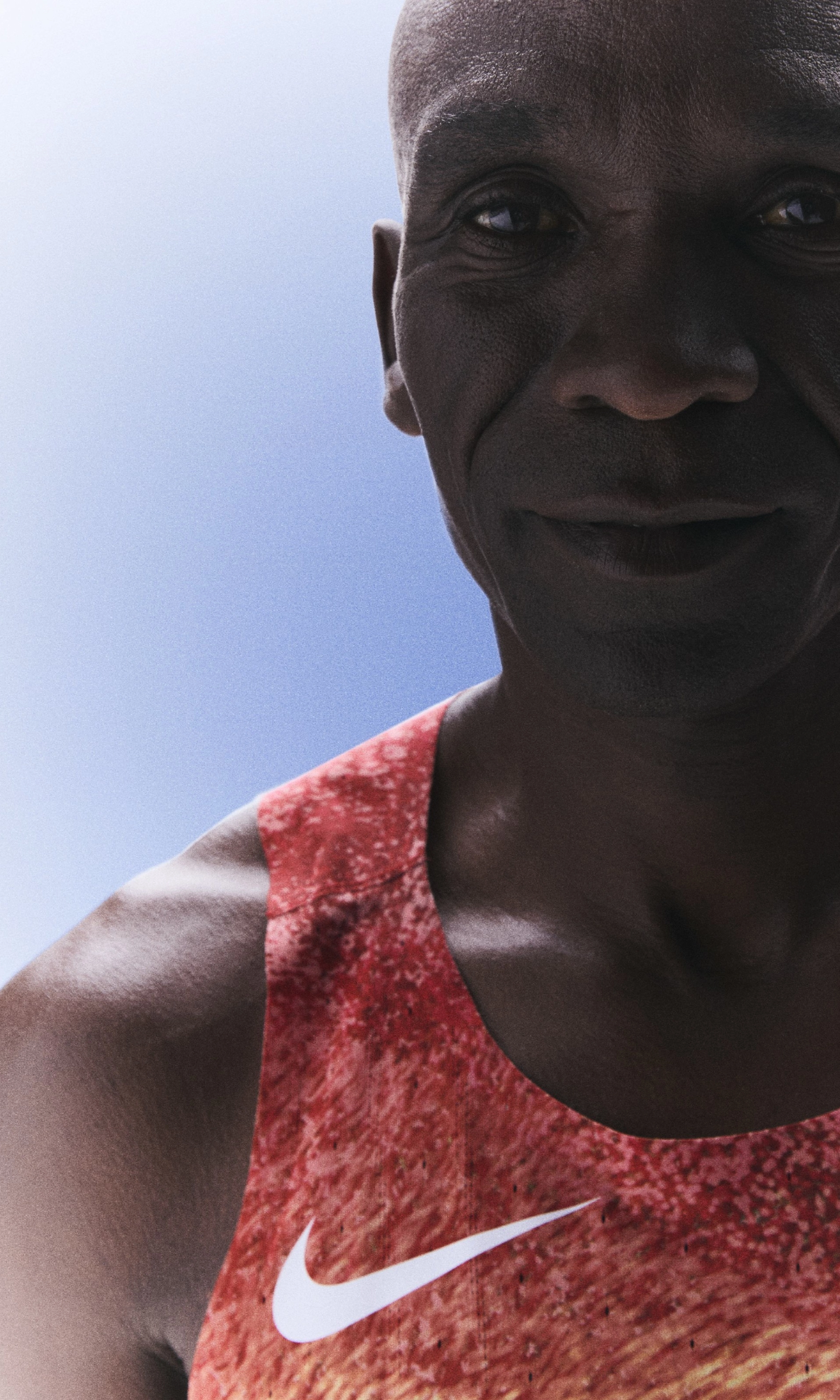 Front upper body view of Eliud Kipchoge smiling and wearing his Kenya track and field kit uniform.