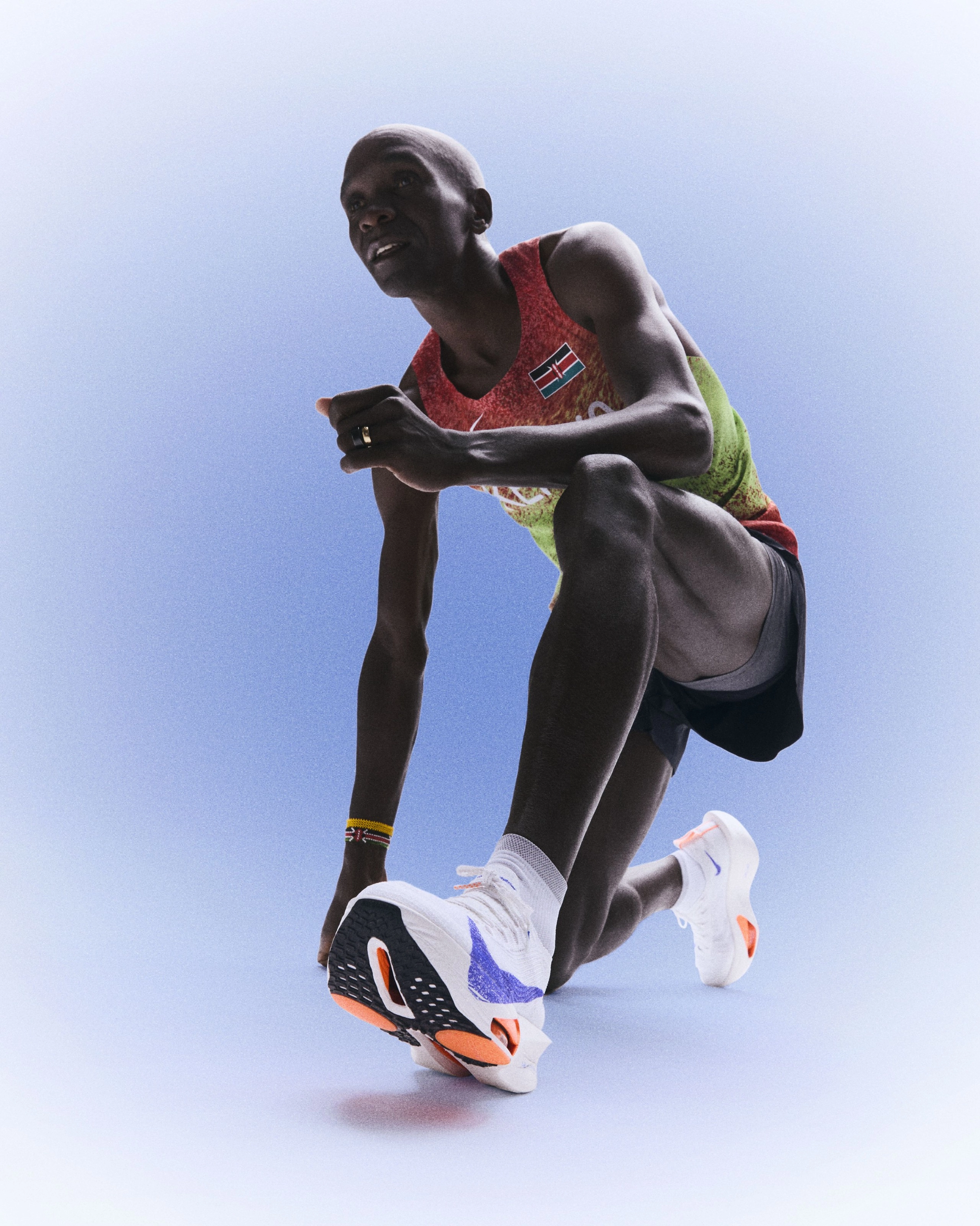 Eliud Kipchoge in a lunge position and looking forward while wearing Kenya's track and field kit uniform.