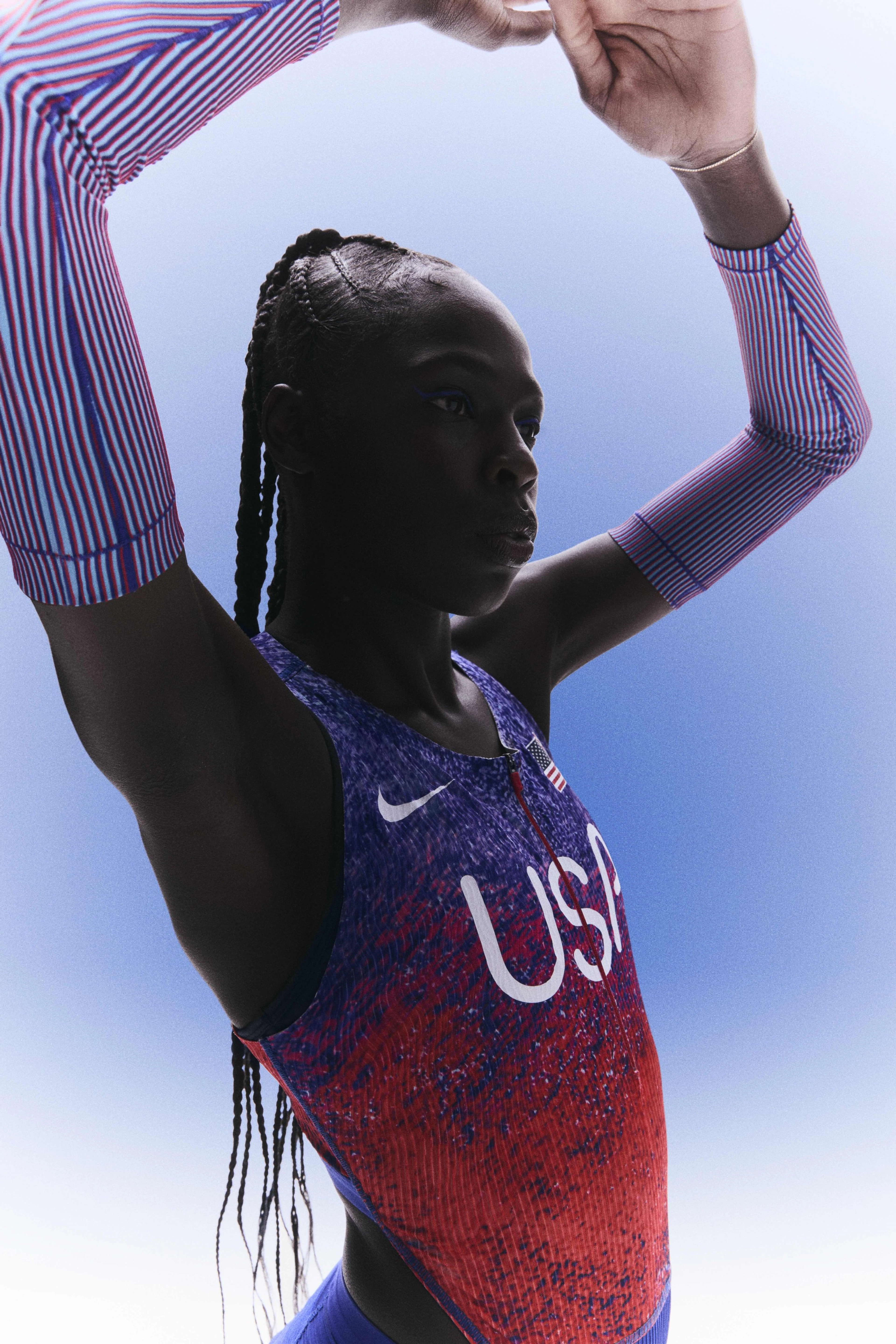 Upper body view of Athing Mu with her hands over her head and wearing her track and field kit uniform.