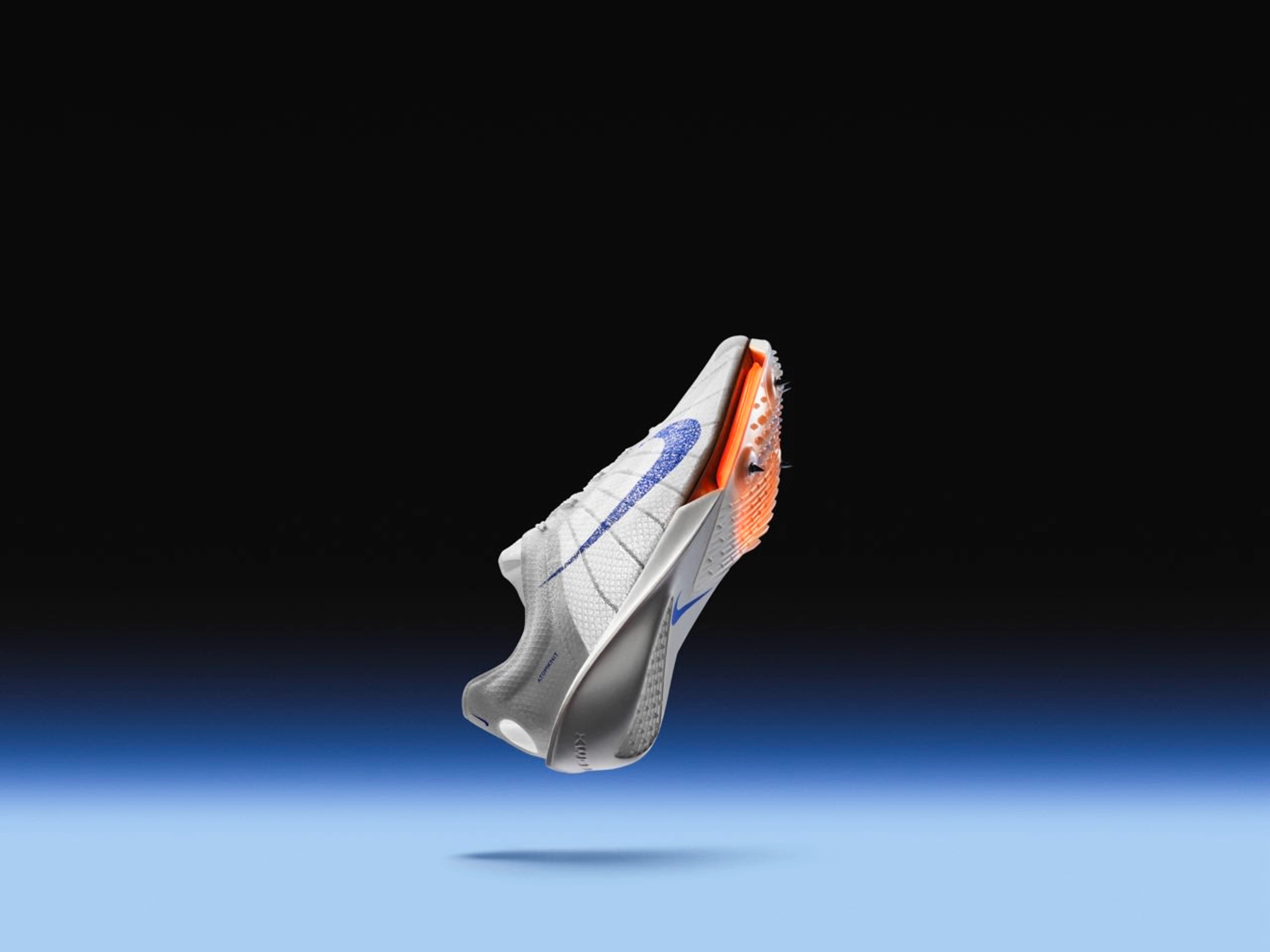 Right view of Nike Victory 2 spike in Blueprint colorway. White upper with a speckled blue Swoosh, orange Air Zoom unit, and a white spike plate. The shoe floats above a blue floor against a black background.