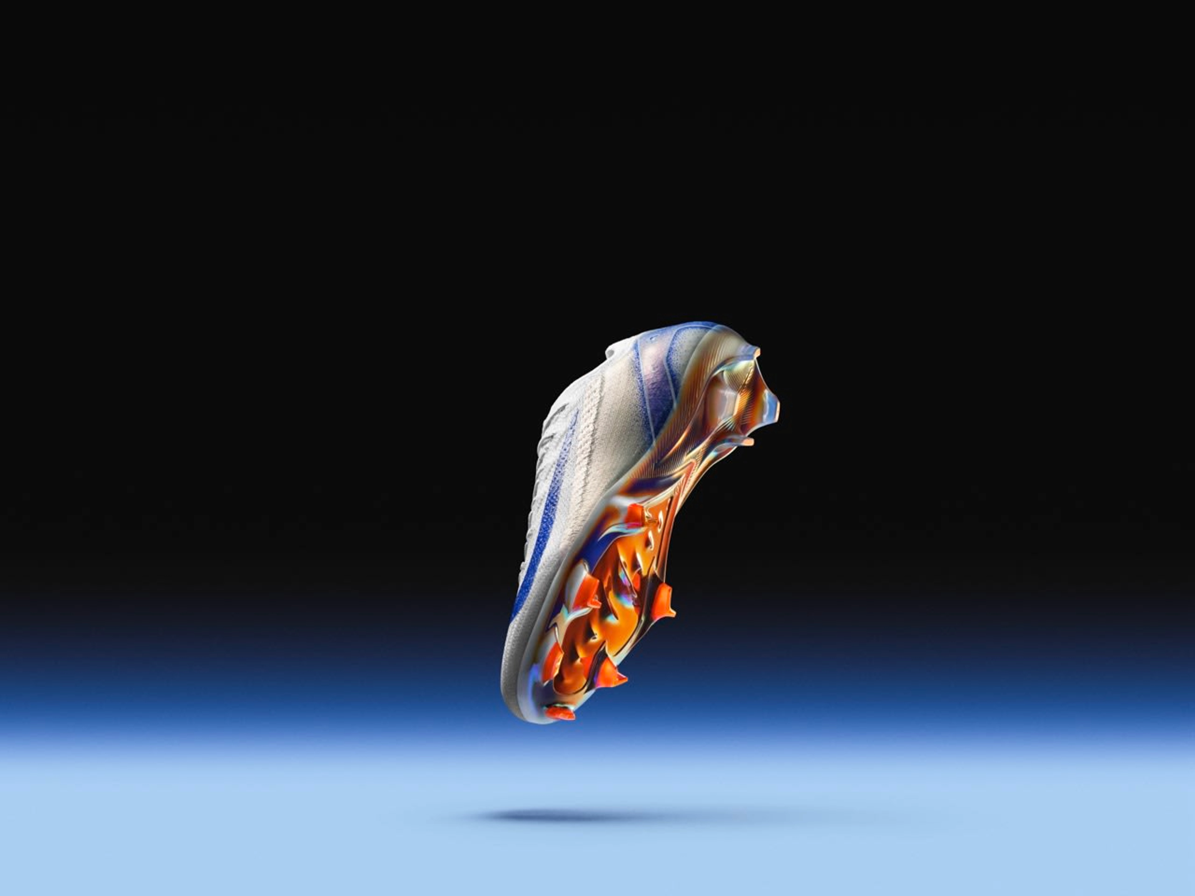 Underside view of a Nike Air Zoom Mercurial Vapor football boot in the Blueprint colorway. White Flyknit upper with a speckled blue Swoosh and iridescent orange cleats and sole plate. The shoe floats above a blue floor against a black background.