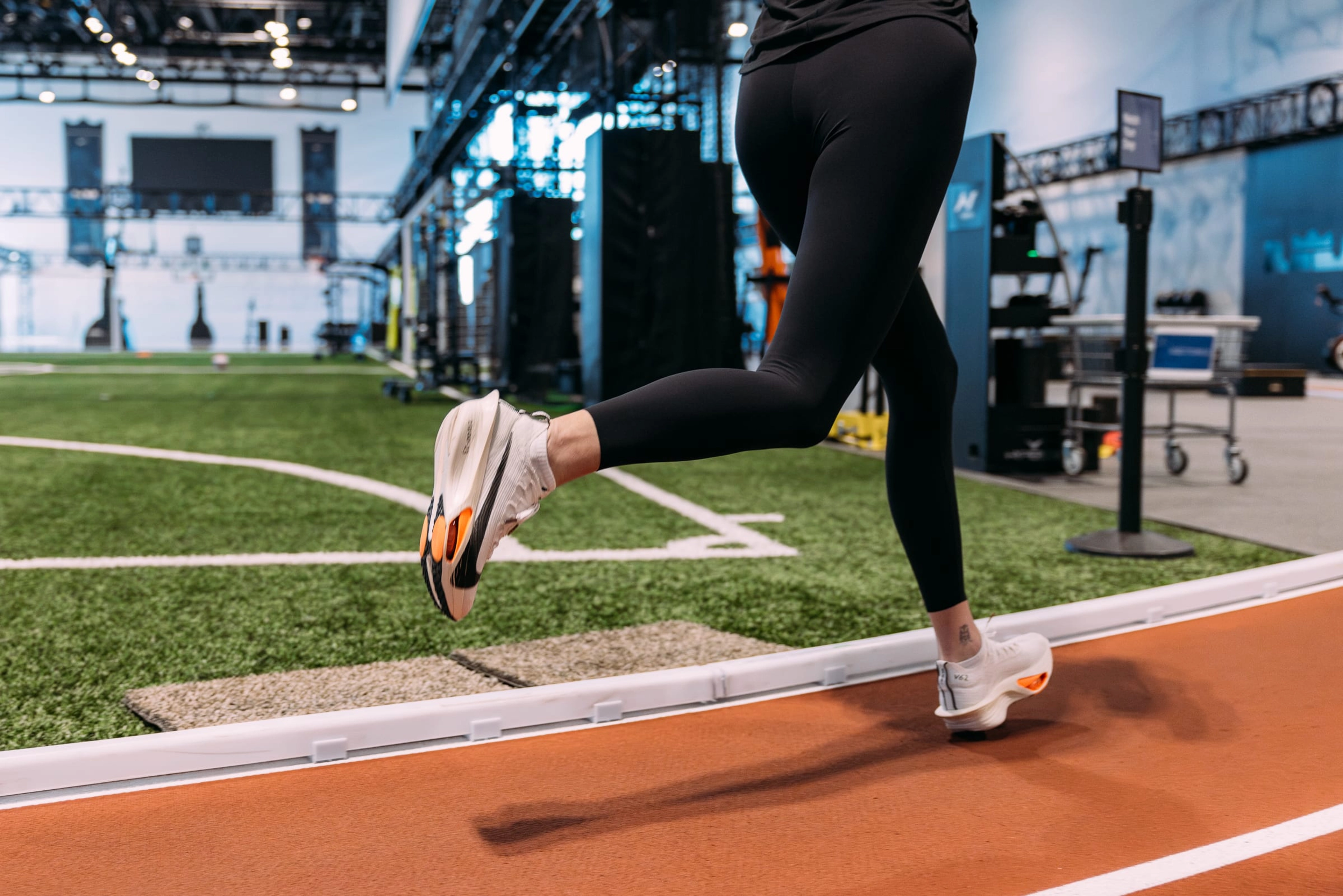 A waist down view of a female runner in black tights tests the Nike Alphafly 3 on the track in the Nike Sports Research Lab. There is scientific equipment in the background.