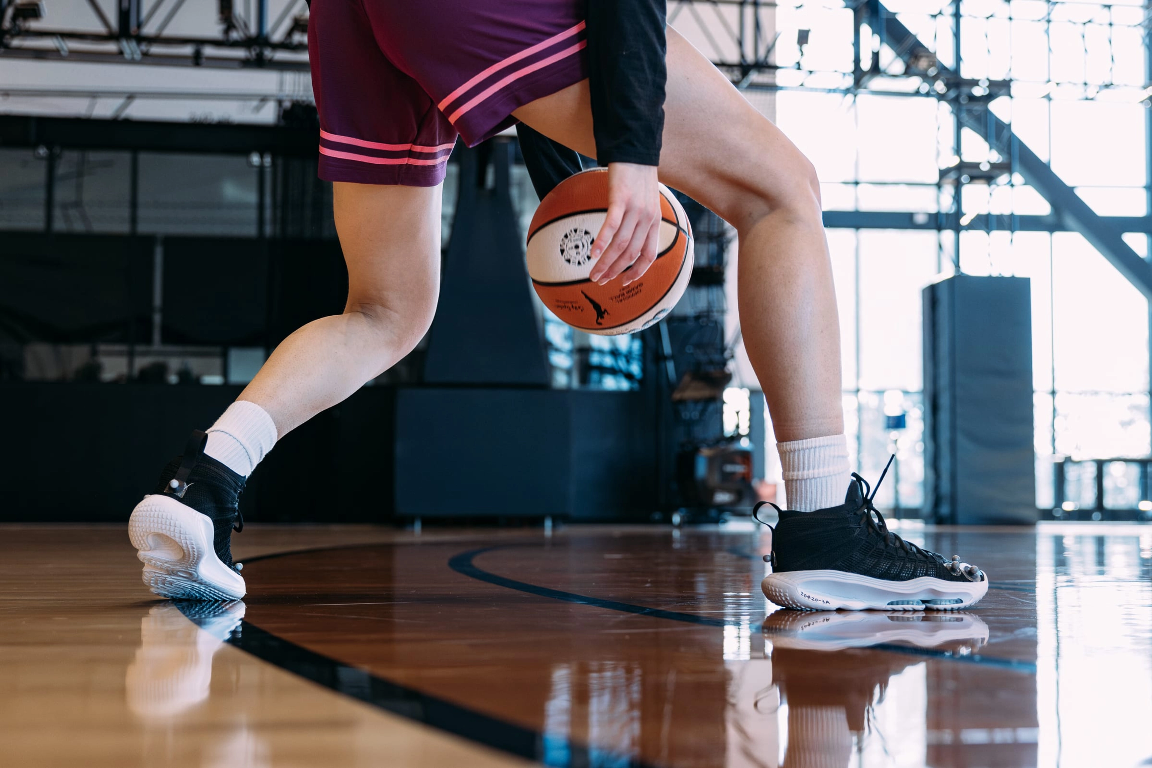 A waist down view of a female basketballer in burgundy shorts, dribbling a basketball while testing the Nike GT Hustle 3 on the basketball court in the Nike Sports Research Lab.