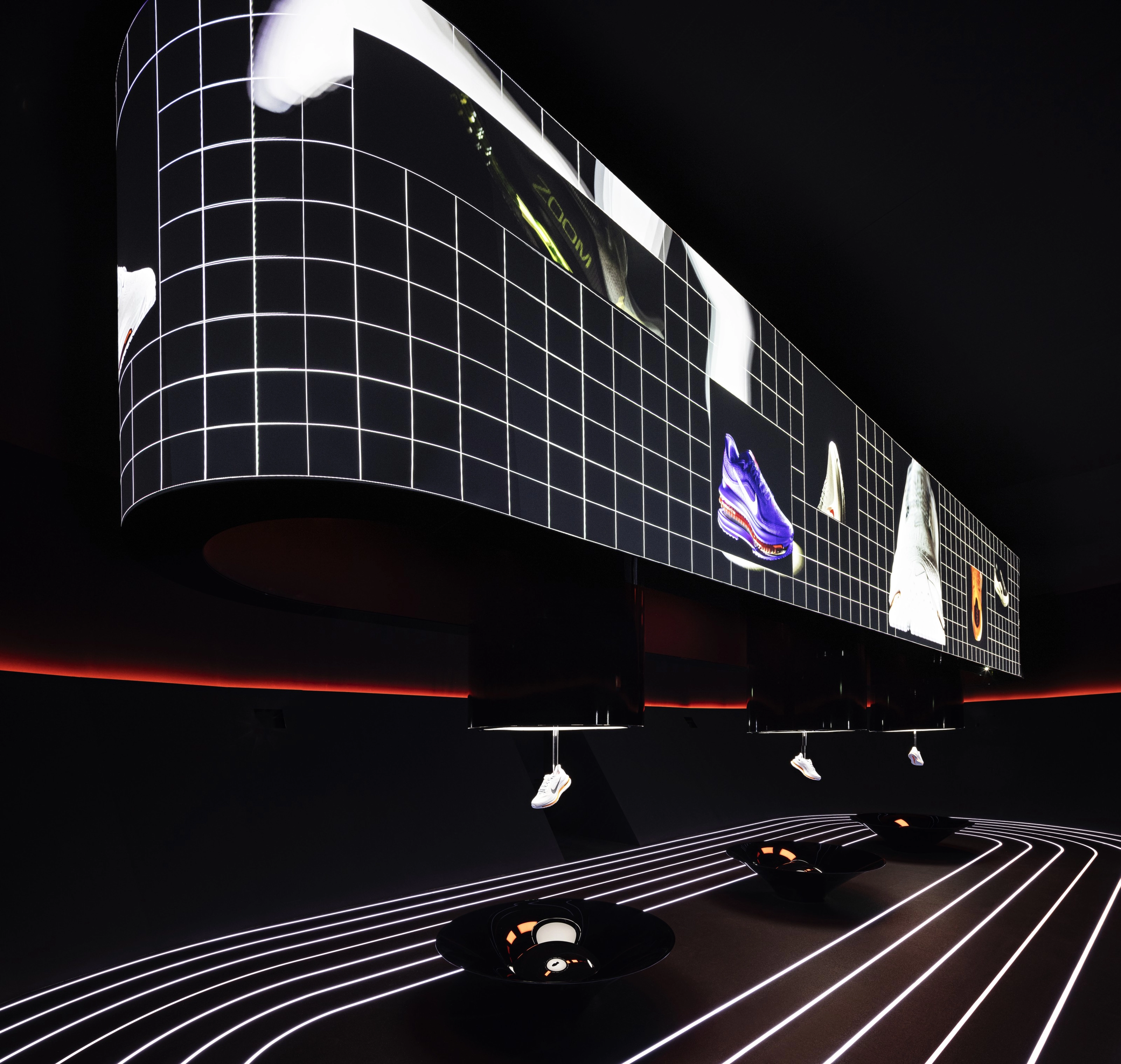 Three Nike sneakers hang from the ceiling in a pitch black room lit only by the lights on the floor and displays.
