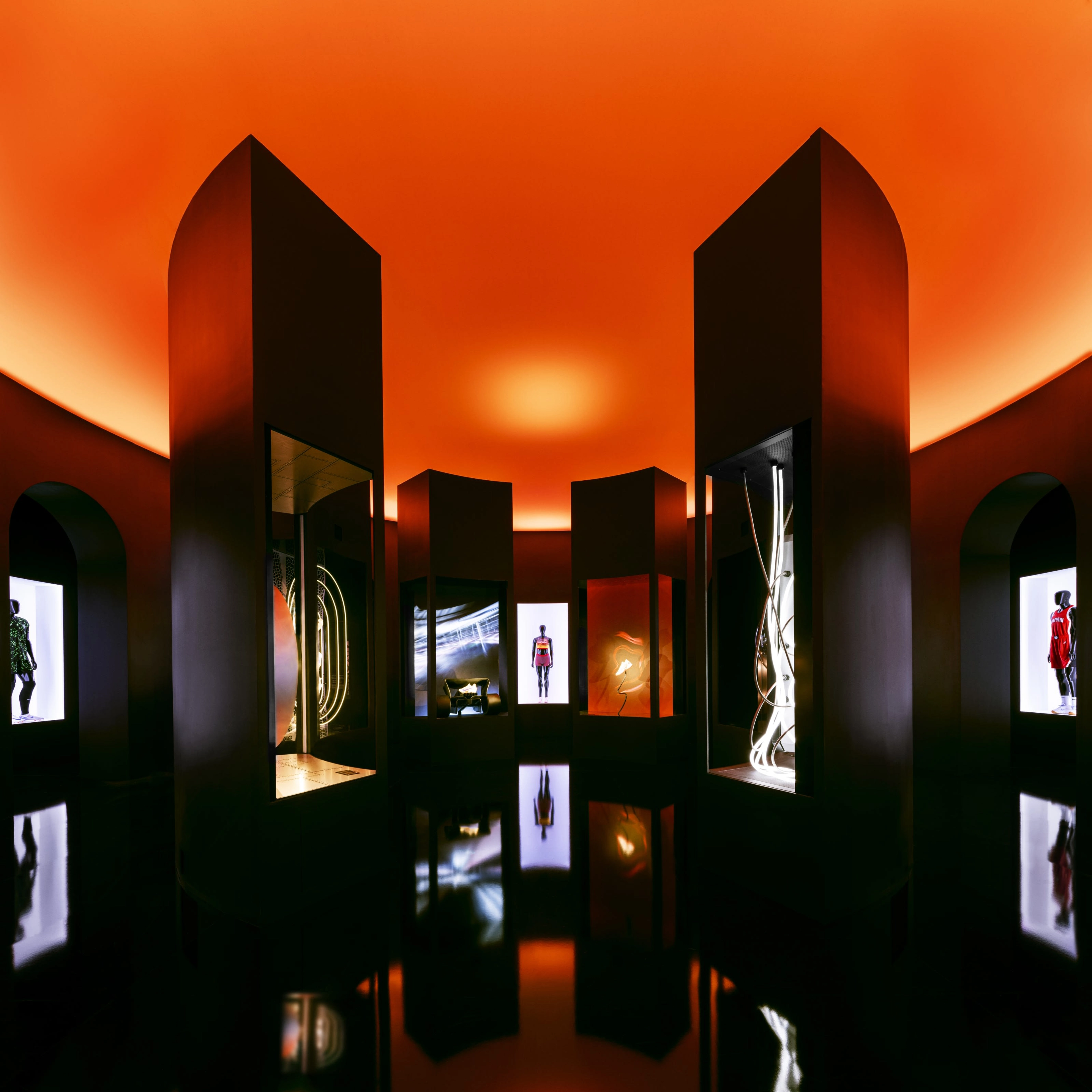 A room with a well polished floor dimly lit in orange light, with artistic displays and mannequins wearing Nike products.
