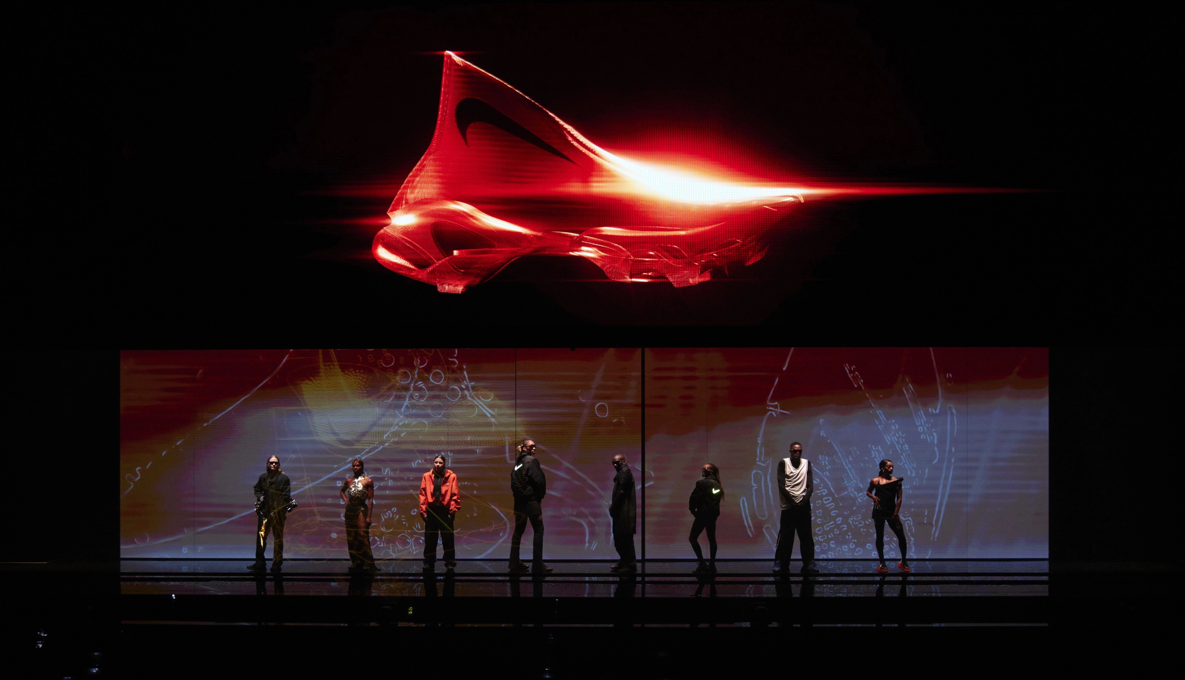 Athletes in dark clothing pose on a dimly lit stage. A crimson red sneaker is displayed on the overhead screen.