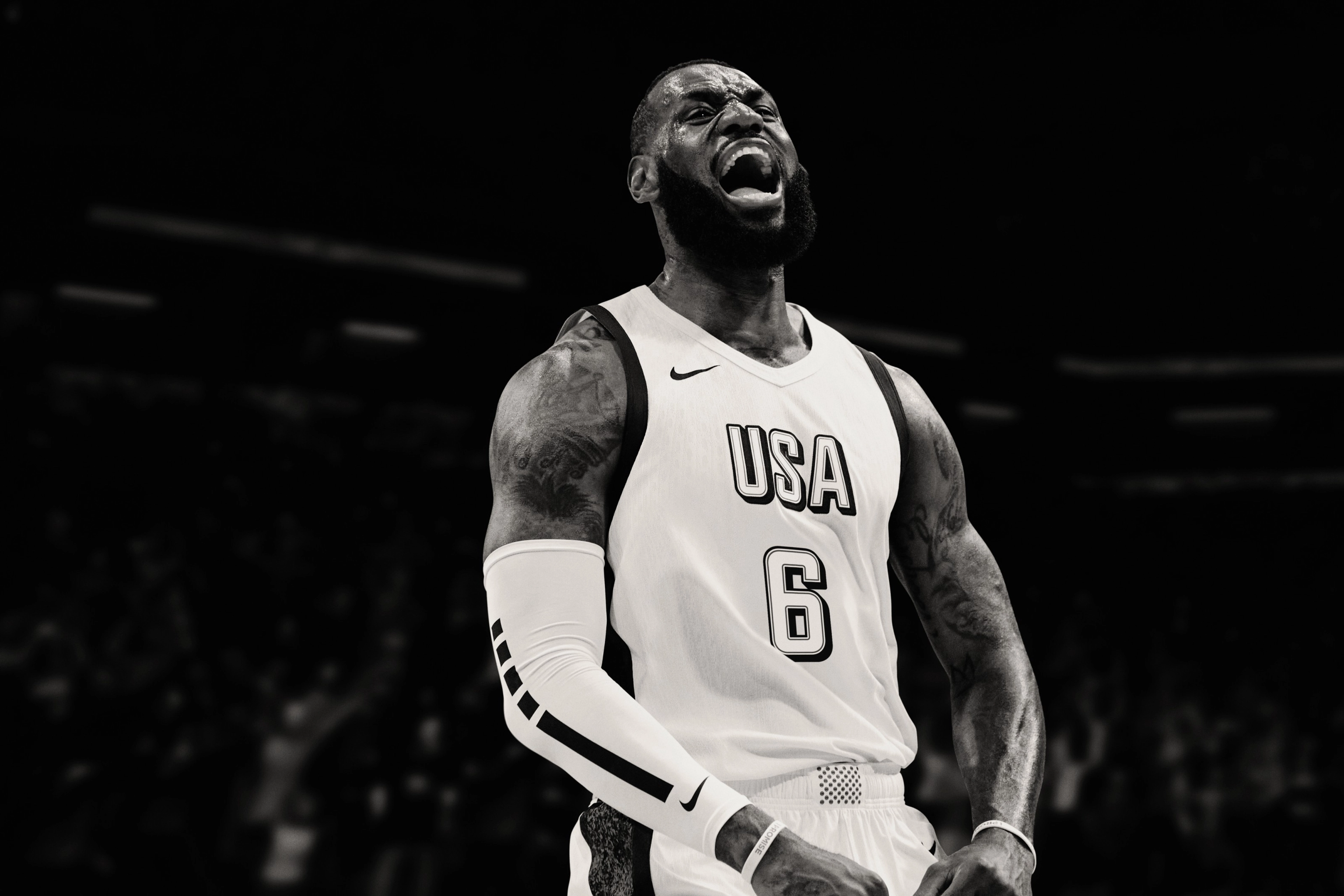 Black and white image of Nike Athlete, Lebron James, wearing Team USA Basketball jersey and a white Nike Pro Elite sleeve. He yells enthusiastically.