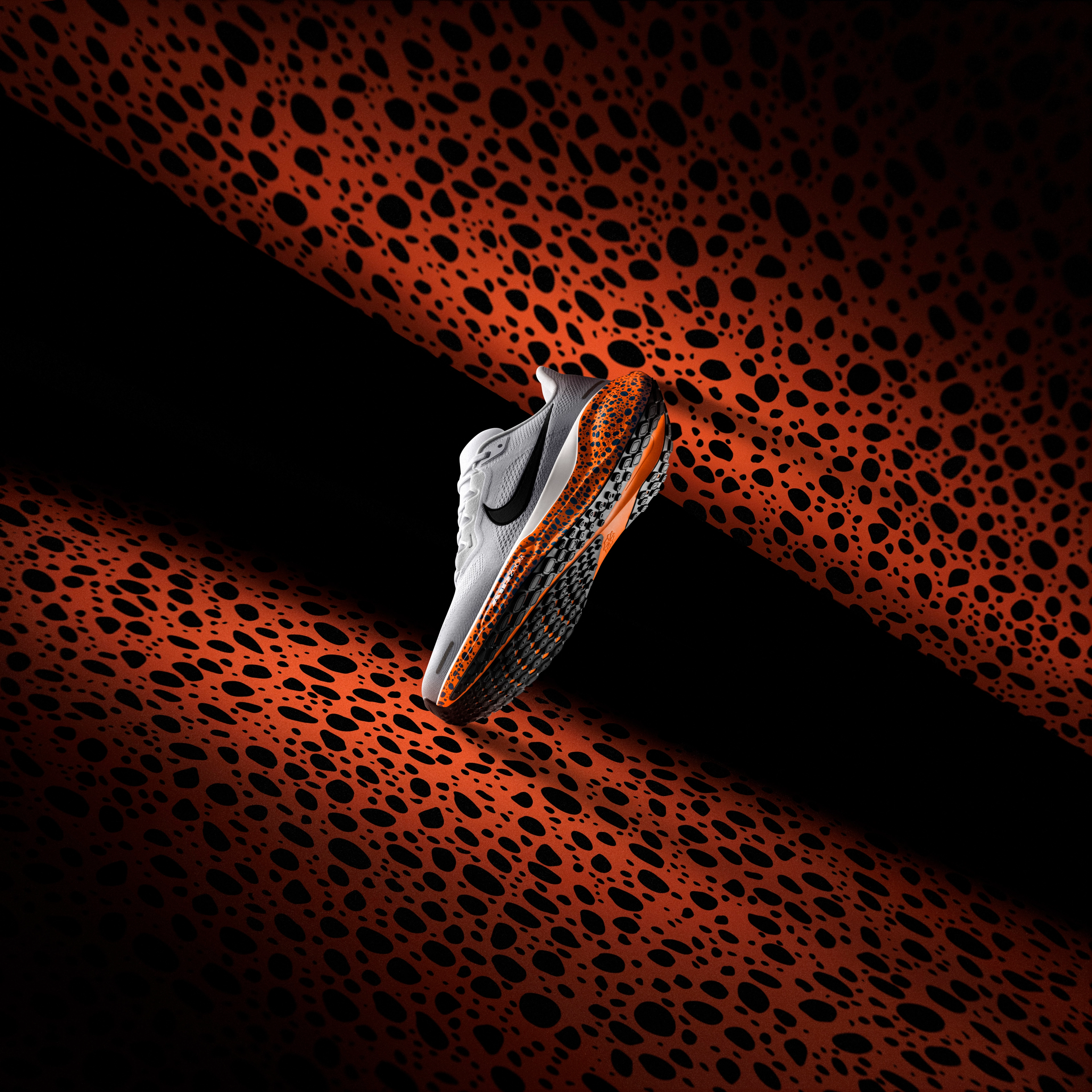Side view of the Nike Pegasus 41 running shoe in the Electric colorway, which is a white upper with a speckled blue/black pattern on the midsole, black Swoosh, and black and orange sole. The shoe sits on an orange Electric pattern background.