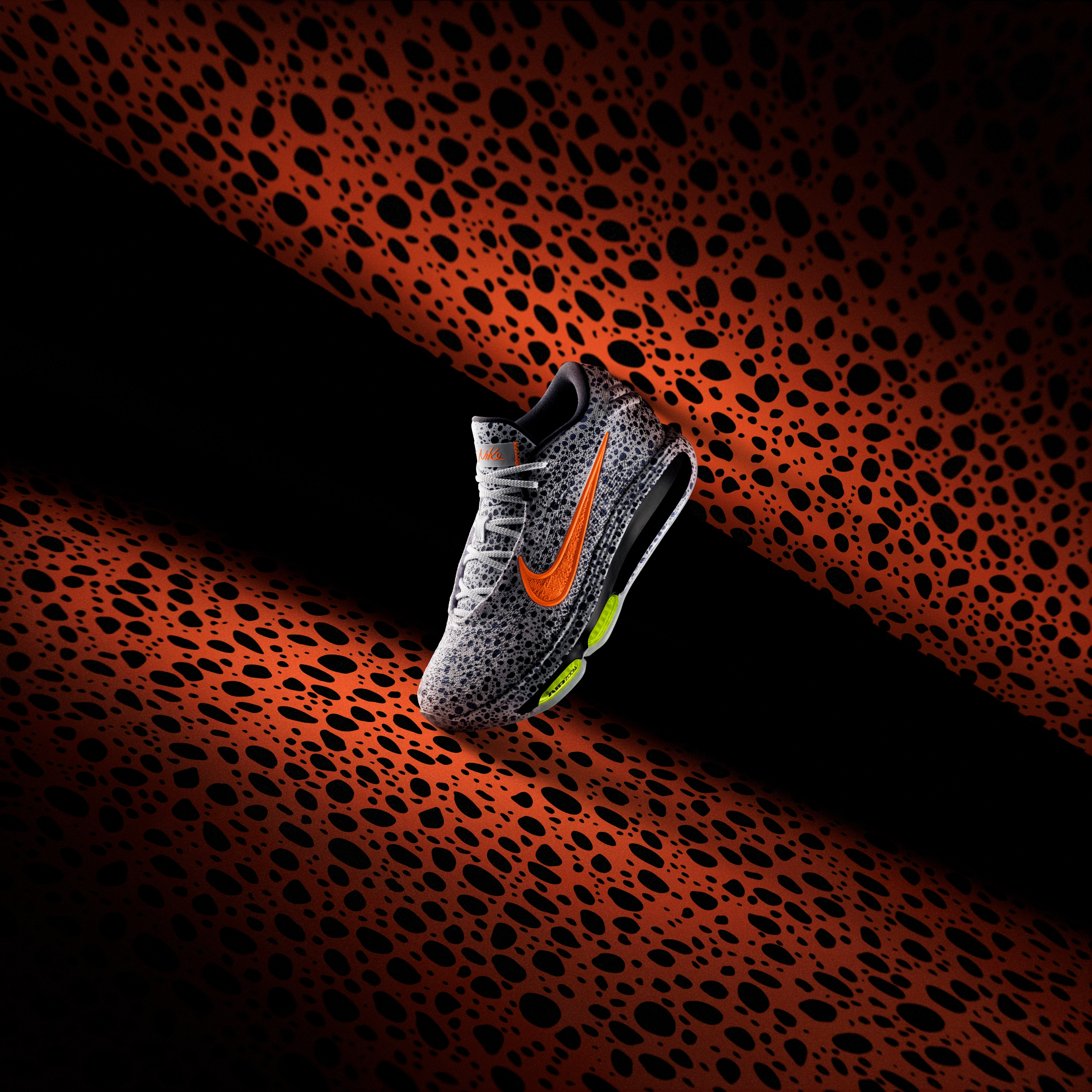 Left view of a Nike GT Hustle 3 basketball shoe in the Electric colorway, which is a gray upper with a speckled blue/black pattern, orange Swoosh, and Volt Air Zoom units. The shoe sits on an orange Electric pattern background.