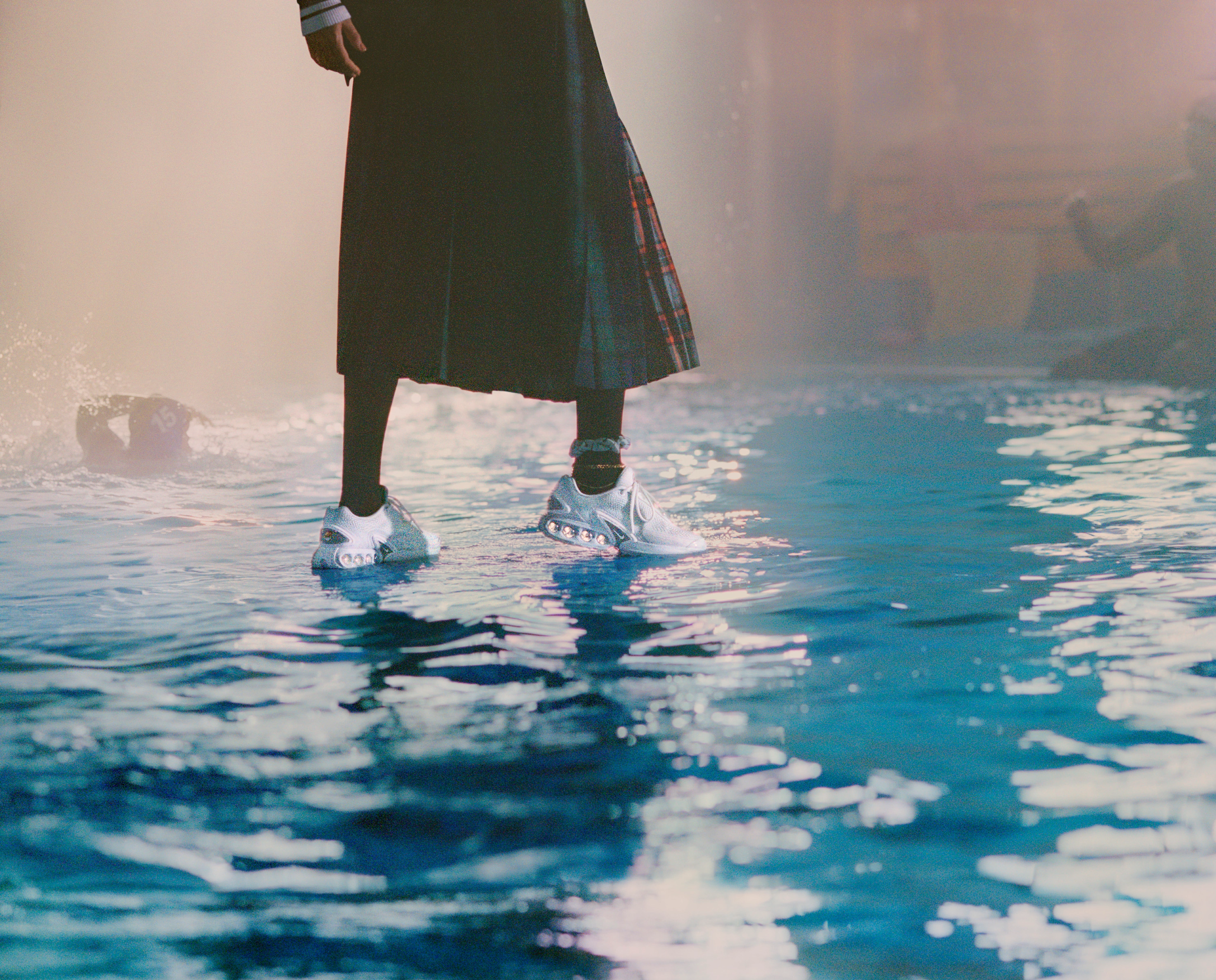 Lower body view of a female model wearing the Nike Air Max Dn in white while walking on water at a pool