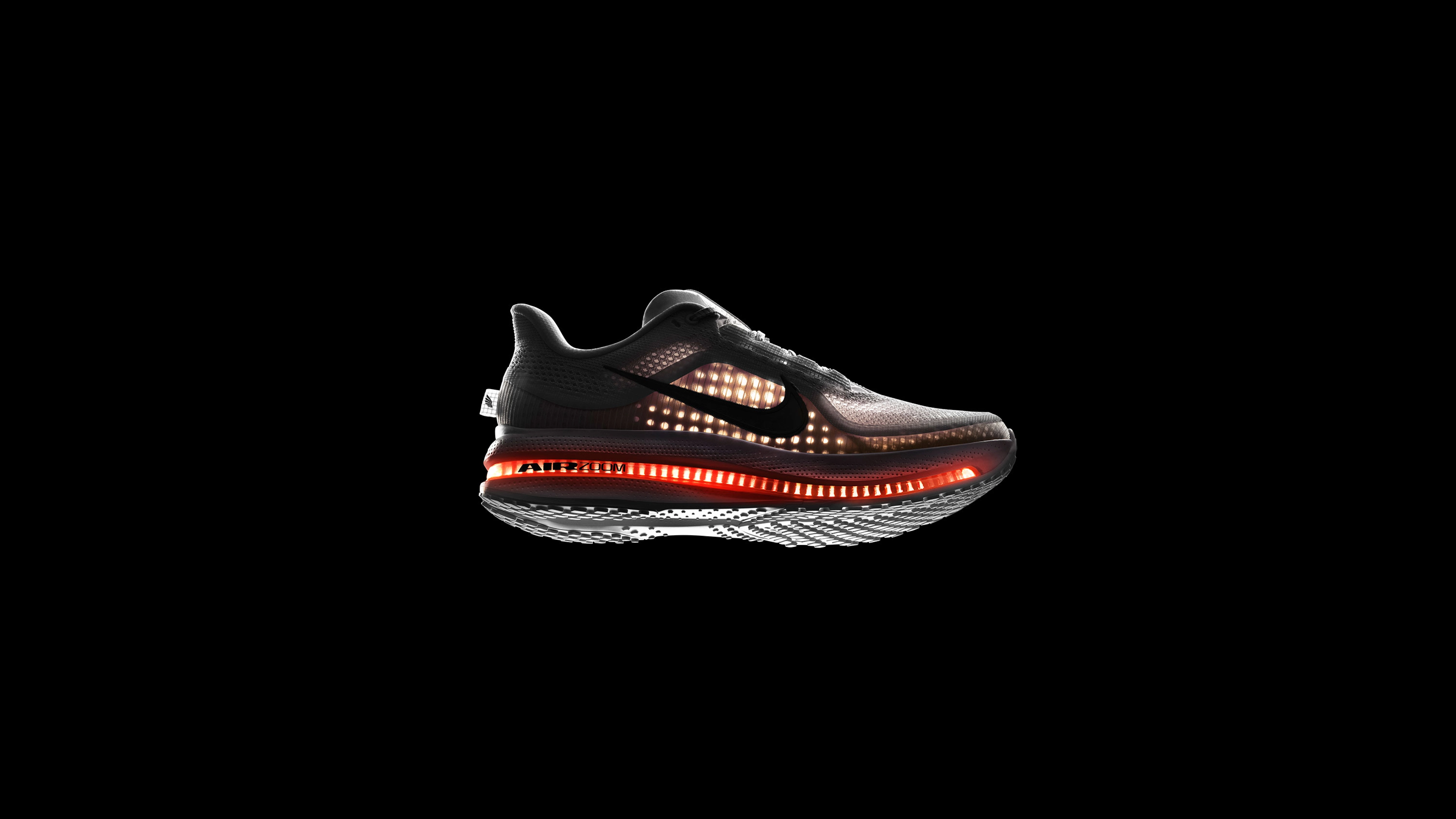 Right view of Nike Pegasus Premiun, backlit against a black background, the shining light allows us to see the visible Air Zoom Unit running the length of the shoe and the breathable circular knit of the upper. White upper, white midsole, orange Air Zoom Unit, white sole, with a black Swoosh.