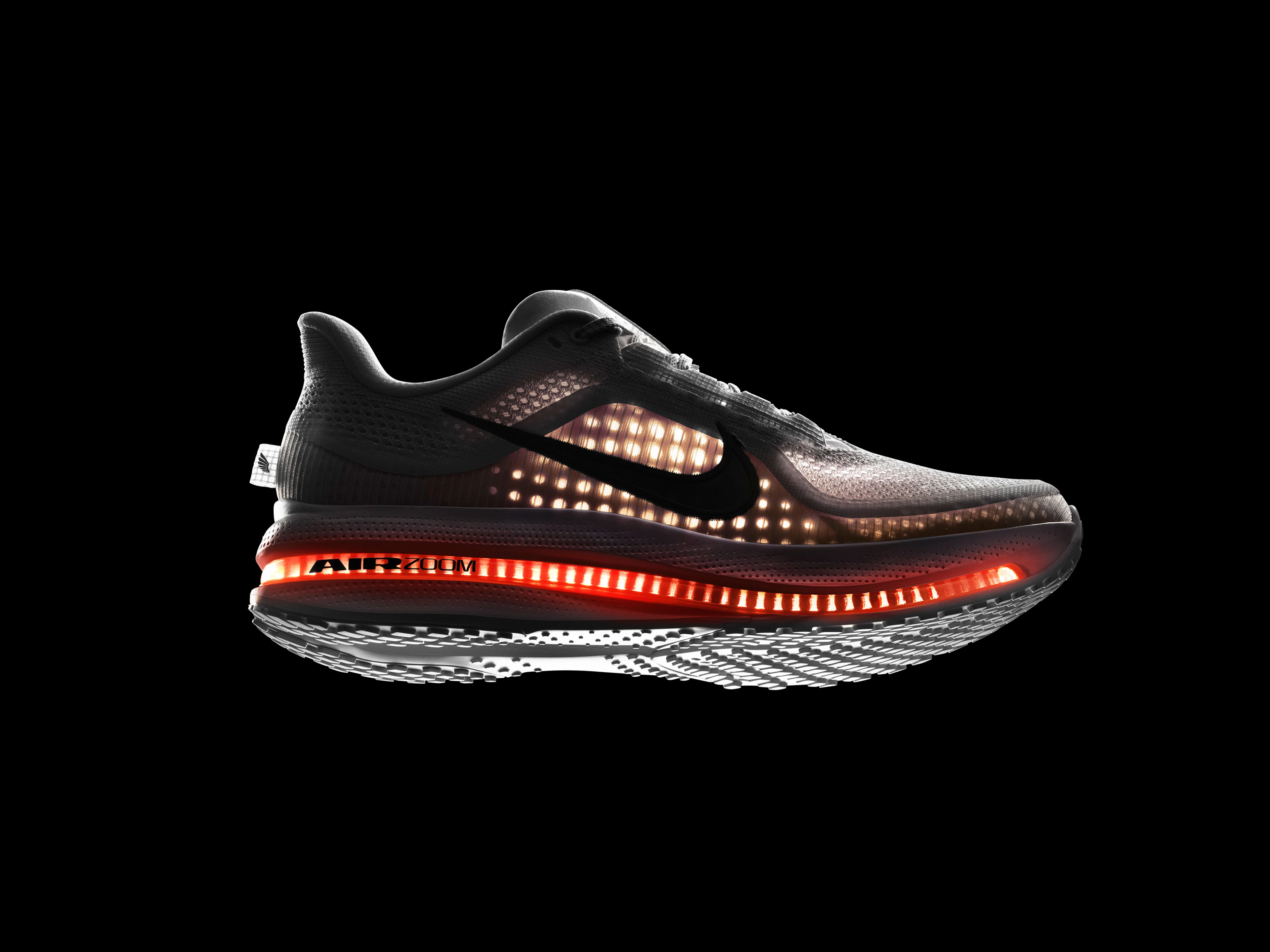 Right view of Nike Pegasus Premiun, backlit against a black background, the shining light allows us to see the visible Air Zoom Unit running the length of the shoe and the breathable circular knit of the upper. White upper, white midsole, orange Air Zoom Unit, white sole, with a black Swoosh.