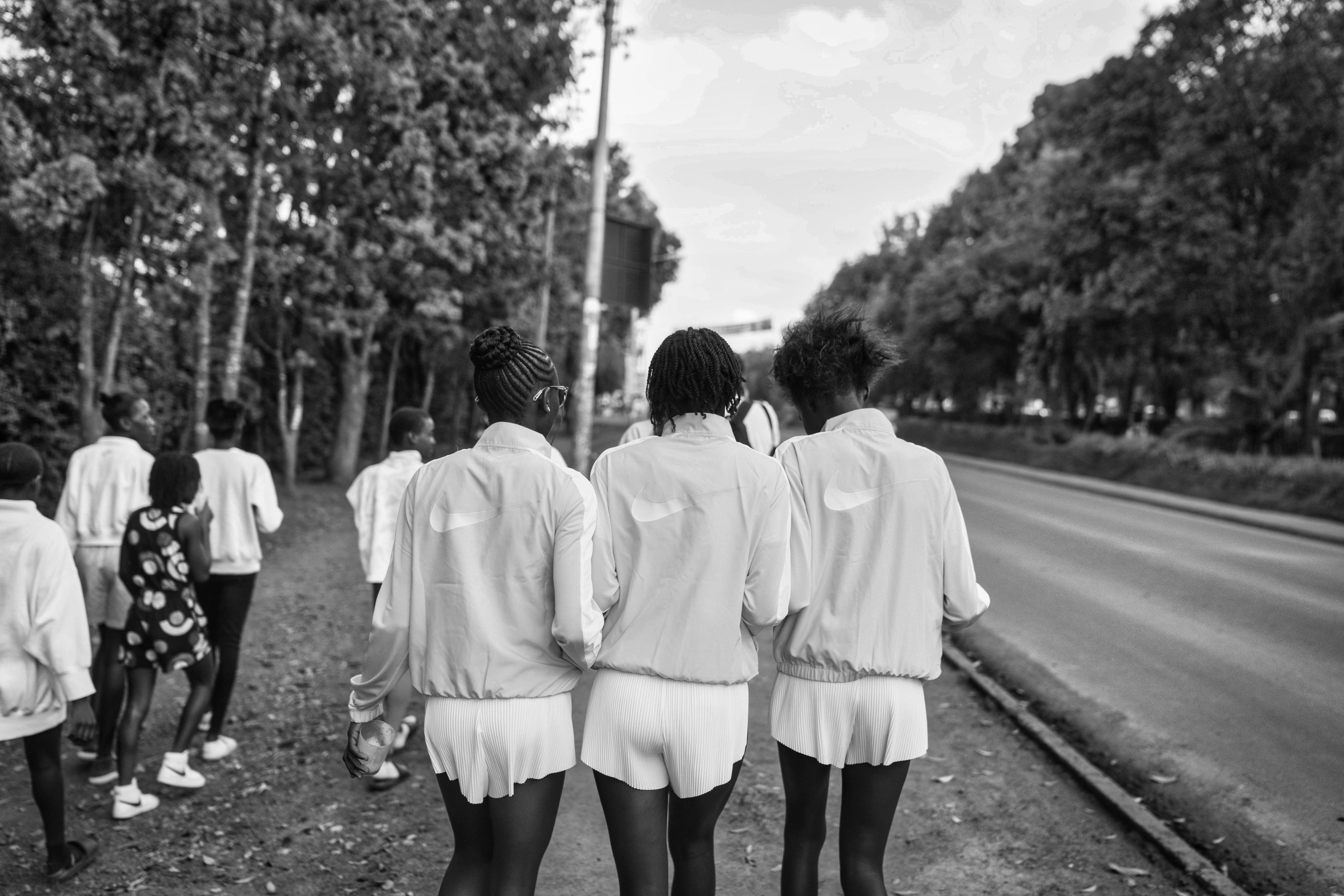 Black and white back view photo of Nala Track Club members walking down the street, 3 of which are walking side by side wearing Nike running jackets.
