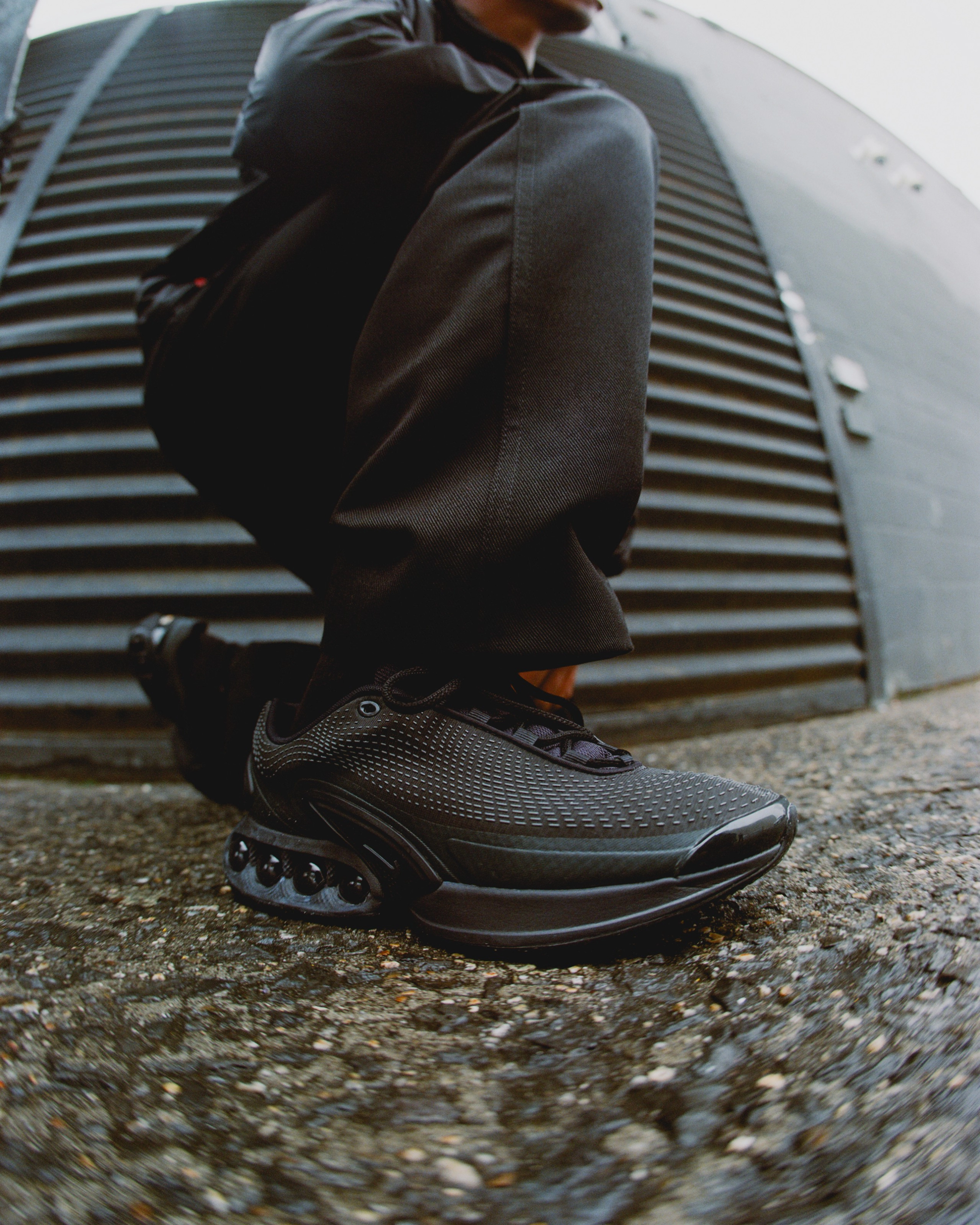 Zoomed in right leg view of a male model down on one knee wearing the Nike Air Max Dn in black