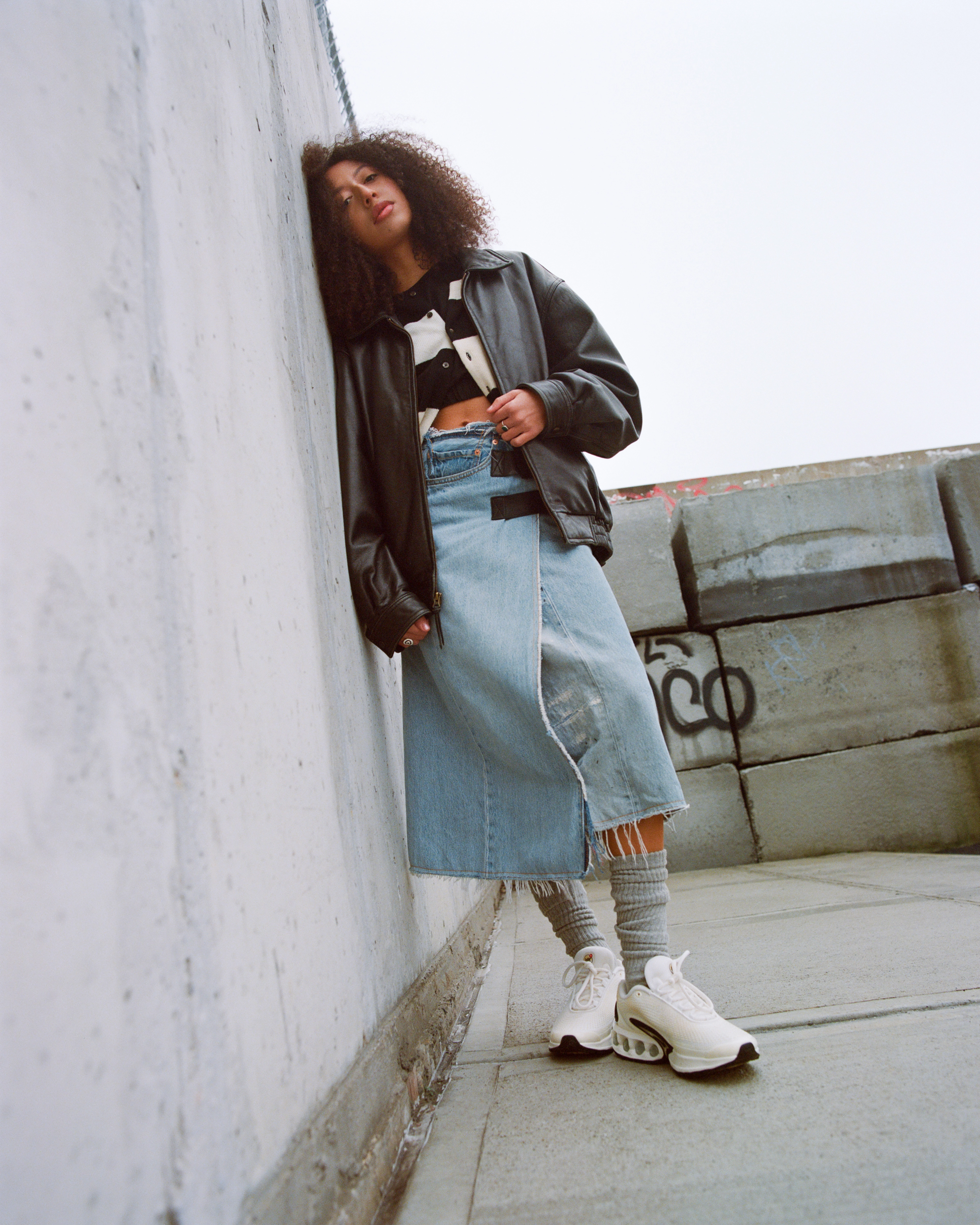 Female model wearing the Nike Air Max Dn in white while leaning her head against a concrete wall outside