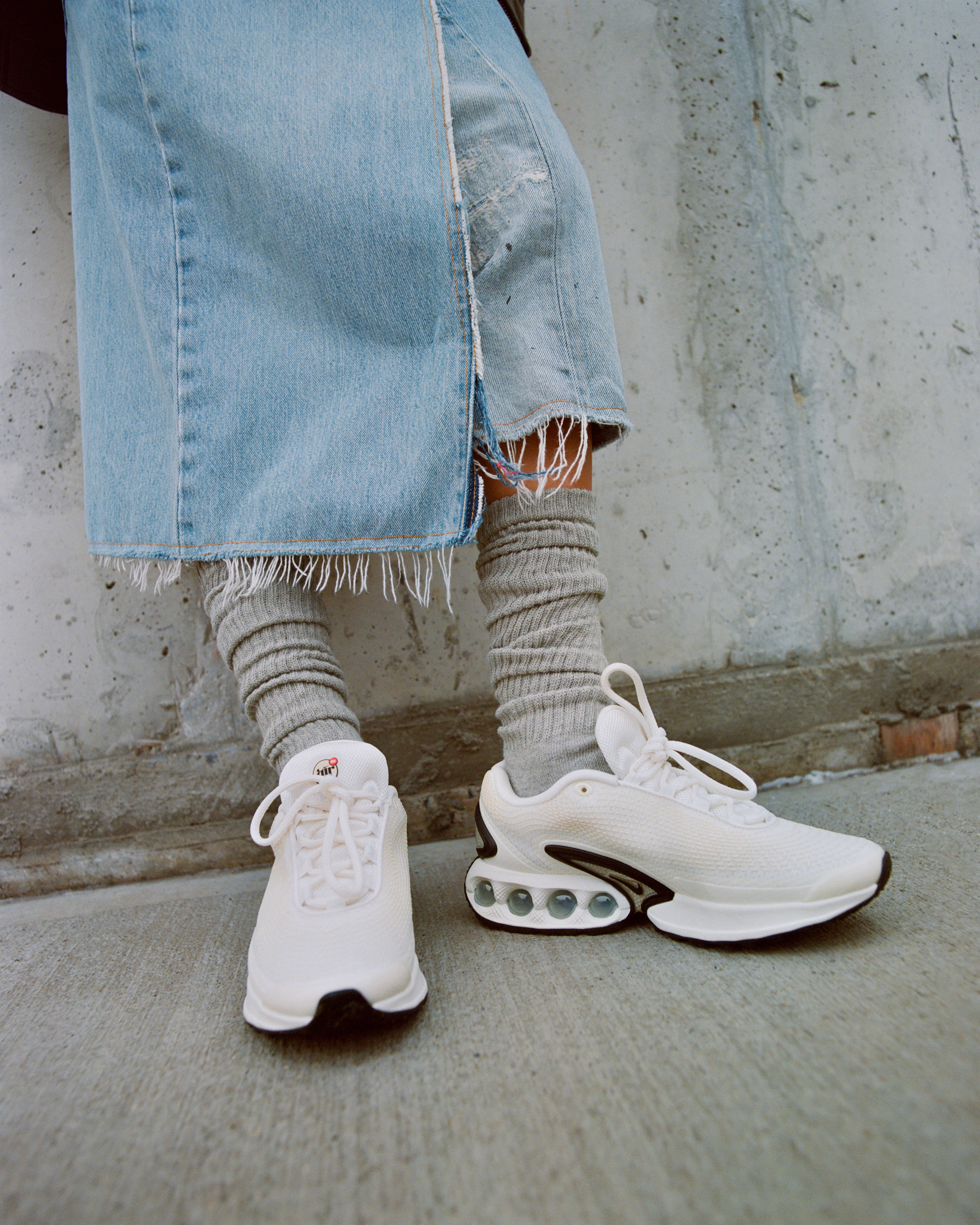 Zoomed in lower view of a model's legs wearing the Nike Air Max Dn in white outside in an industrial area
